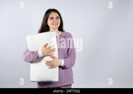 Bella donna brunetta in mussola porpora pigiama pigiami dormiente tiene un cuscino ortopedico, un posto per il testo Foto Stock