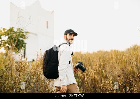 Ritratto di un giovane barbuto, con cappuccio nero, con la sua fotocamera digitale in campagna Foto Stock