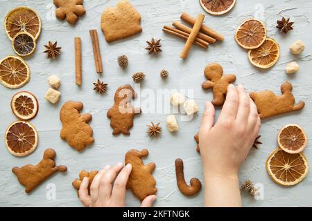 Le mani femminili contengono biscotti di pan di zenzero. Diversi tipi di biscotti e spezie natalizie su sfondo grigio, vista dall'alto. Foto Stock