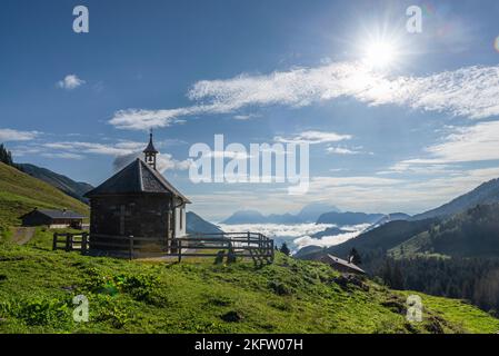 La cappella sul Ackernalm di fronte ai monti Kaiser, alla luce del sole del mattino, Tirolo, Austria Foto Stock