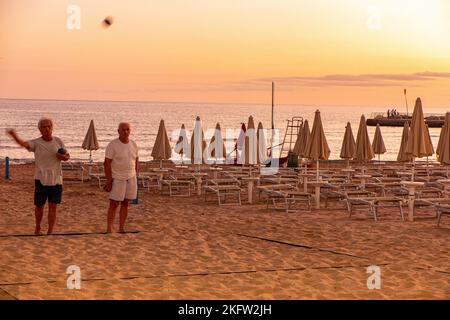 Due uomini maturi si divertiranno a giocare a bocce sulla spiaggia alla fine della giornata Foto Stock