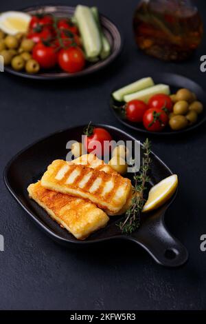 Alloumi alla griglia in una padella nera con olive, pomodori, cetrioli, timo e limone. Formaggi tradizionali del Mediterraneo orientale. Foto Stock