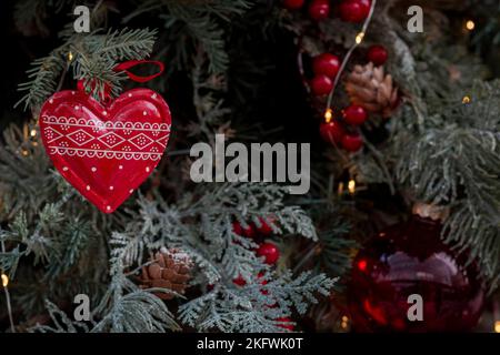 Tradizionale closeup ornamento di Natale a forma di cuore intagliato appeso al ramo di un albero di Natale con luci fata sullo sfondo Foto Stock