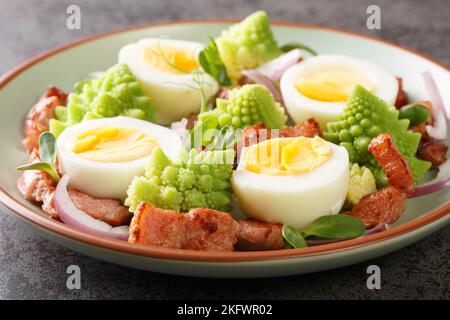 Insalata fatta in casa di cavolo romanesco al vapore, uova sode, pancetta fritta e microgreens freschi primo piano in un piatto sul tavolo. Orizzontale Foto Stock
