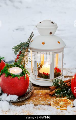 Lanterna bianca nel giardino d'inverno, mele, abeti e neve sul banco di legno. Foto Stock