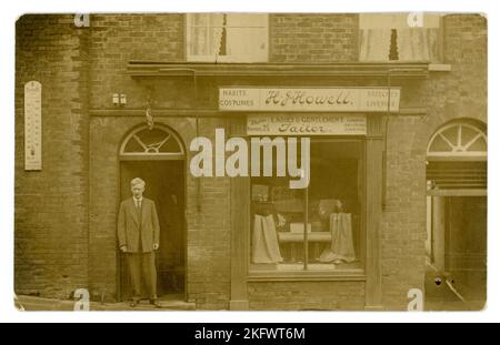 Cartolina originale dell'era WW1 del proprietario/sarto elegantemente vestito, in piedi nella porta fuori un negozio boutique - ci è un segno per impermeabilizzazione di Burberry nella finestra e le lunghezze di tweed. Il segno sopra dichiara H J Howell Ladies and gentes sarti & anche pubblicità sartoria di 'costumi, abitudini., braghe & liveries' il segno inoltre fa pubblicità ad altri locali a 11 Milk St Cheapside London. Ma c'è una centrale telefonica sul cartello per Arundel 25 - così questo negozio si trova nella città costiera del Sussex occidentale di Arundel in High Street - forse si è ritirato qui e ha conservato il negozio di Londra. Circa 1917, Regno Unito Foto Stock