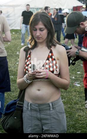 YOUNG WOMAN, CLUBBER, LEGACY MOBILE PHONE, BIKINI TOP, HOMELANDS 2003: Young Woman in a bikini top texting on a legacy mobile phone at Homelands Festival vicino Winchester, Inghilterra, 24 maggio 2003. Fotografia: ROB WATKINS. INFO: Homelands Festival è stato un importante festival di musica elettronica del Regno Unito tenuto in Inghilterra tra la fine degli anni '1990 e l'inizio degli anni '2000 Celebrando la cultura della musica dance, ha caratterizzato i migliori DJ e spettacoli dal vivo di generi come House, drum and bass e techno, attirando folle appassionate. Foto Stock