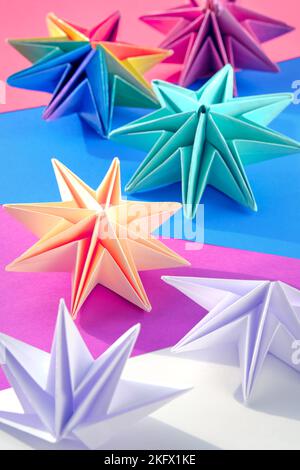 Vibranti stelle di carta origami, decorazioni natalizie fai da te fatte a mano. Stelle natalizie fatte da soli realizzate in carta colorata su sfondo stratificato. Fatto a mano Foto Stock