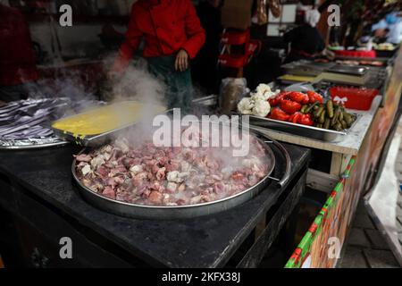 Profondità di campo bassa (fuoco selettivo) dettagli con una grande padella con carne, con polenta e sottaceti vicino, a Bucarest, Romania. Foto Stock