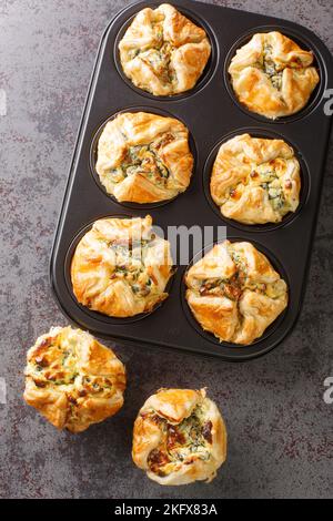 Muffin di spinaci e feta in pasta sfoglia closeup nella forma di cottura di impaffina sul tavolo. Vista verticale dall'alto Foto Stock