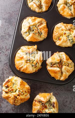 Muffin di pasta sfoglia ripieni di spinaci e formaggio feta primo piano in una teglia per muffin sul tavolo. Vista verticale dall'alto Foto Stock