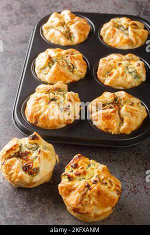 Muffin di pasta sfoglia ripieni di spinaci e formaggio feta primo piano in una teglia per muffin sul tavolo. Verticale Foto Stock