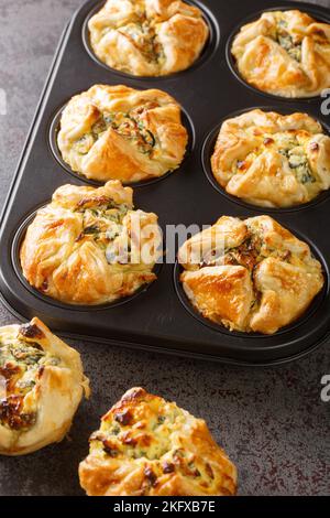 Muffin di spinaci e feta in pasta sfoglia closeup nella forma di cottura di impaffina sul tavolo. Verticale Foto Stock