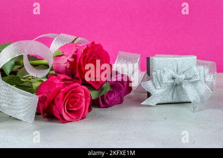 Sfondo celebrativo di rose e una scatola regalo argentata con nastro, primo piano con posto per il testo Foto Stock