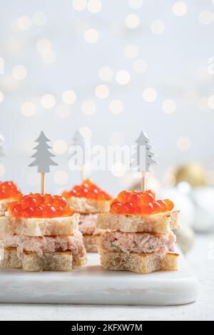 Canape all'albero di Natale con salmone affumicato, formaggio cremoso, aneto, piatto di rafano e caviale rosso per uno spuntino natalizio Foto Stock