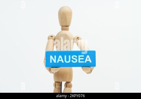 Concetto di medicina e assistenza sanitaria. Una figurina di un uomo tiene in mano un blocco di legno blu con l'iscrizione NAUSEA. Il figurine è fuori fuoco. Foto Stock