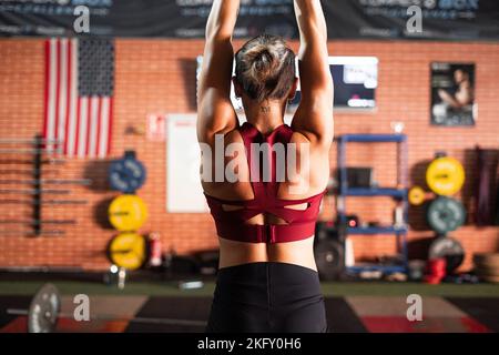 brunetta muscolare ragazza caucasica sulla schiena con le braccia distese facendo sport in palestra Foto Stock