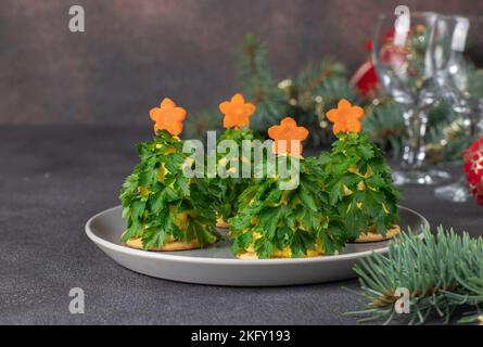 Spuntino festivo sotto forma di albero di Natale a base di formaggio, uova sode, prezzemolo e stelle di carota su sfondo grigio Foto Stock