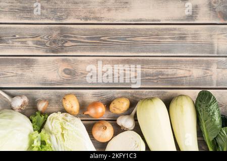 Composizione alimentare vegana di cipolla, cavolo, zucchine, midollo di zucca, verdure all'aglio su fondo ligneo. Negozio di alimentari. Prodotti agricoli vegetariani Foto Stock