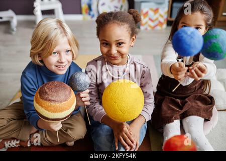 Gruppo di adorabili bambini multiculturali che studiano pianeti del sistema solare mentre tengono i loro modelli a lezione di astronomia in asilo Foto Stock