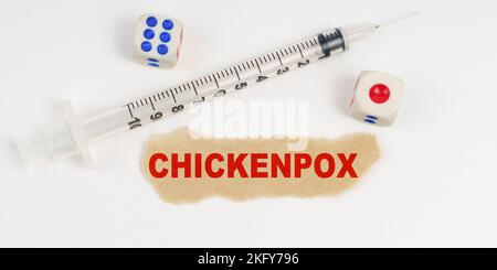 Concetto medico. Su una superficie bianca si trova una siringa, un dado e un pezzo di carta con l'iscrizione - VARICELLA Foto Stock