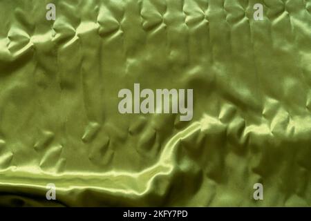 tessuti di raso giallo-verde adagiati sul pavimento con un po' d'acqua e rughe Foto Stock