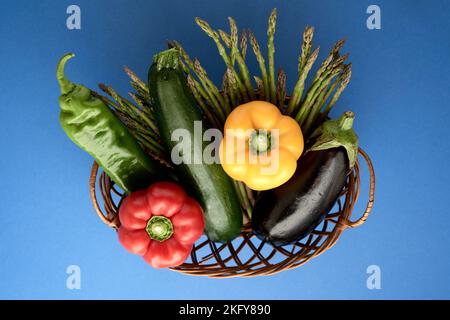 primo piano di un cesto di vimini pieno di verdure su sfondo blu Foto Stock