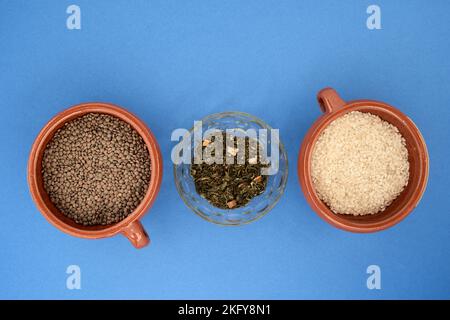 primo piano di tre contenitori contenenti legumi e cereali commestibili su sfondo blu Foto Stock