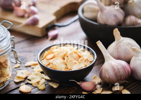 Ciotola di fiocchi d'aglio secchi. Teste di aglio, vaso di vetro di fiocchi d'aglio sul tavolo da cucina. Condimento essiccato. Foto Stock