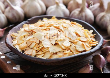 Ciotola di fiocchi d'aglio secchi, spicchi d'aglio. Teste di aglio sullo sfondo. Condimento essiccato. Foto Stock