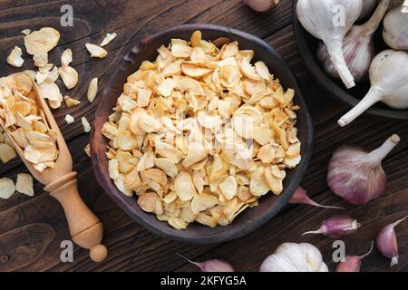 Ciotola di fiocchi d'aglio secchi, spicchi d'aglio. Teste di aglio sul tavolo da cucina. Vista dall'alto, disposizione piatta. Foto Stock