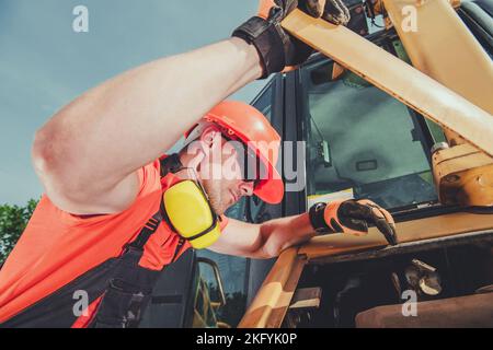 Operatore dell'escavatore professionale che verifica le condizioni del motore della macchina. Tema macchine industriali per impieghi pesanti. Foto Stock