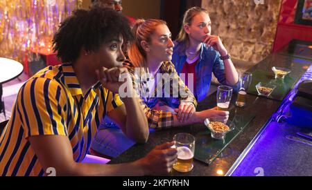 Quattro amici maschi e femmine, diversi e tesi, che guardano una partita di sport in un bar Foto Stock