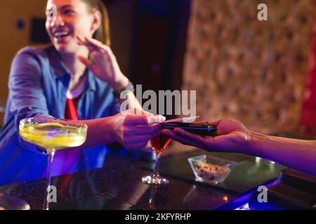 Donna caucasica sorridente che paga barman per un drink con carta di credito al bar Foto Stock