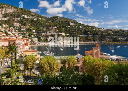 Appartamenti colorati e facciate di benvenuto dell'edificio alberghiero e del porto con barche da diporto e barche a vela ancorate nella baia, Villefranche-sur-Mer, Provenza. Foto Stock