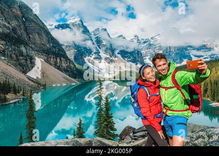 Moraine lago coppia turisti che scattano foto selfie sul Canada escursione di viaggio utilizzando il telefono. I giovani escursionisti sono felici di usare il telefono durante le vacanze a Banff Foto Stock