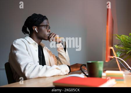 Il computer concentrato di successo dell'uomo afro-americano si siede sul posto di lavoro con la tazza di caffè Foto Stock