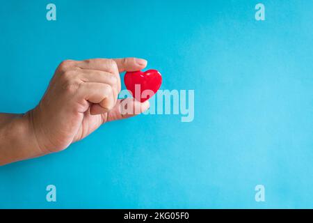 Concetto di salute del cuore. Dito dell'uomo che tiene una forma a cuore rosso. Spazio di copia. Foto Stock