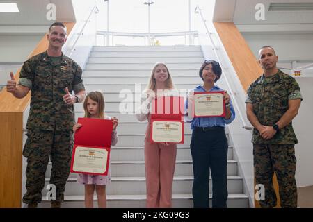 Paul C. Cordes, il Marine Corps Air Station Iwakuni executive officer, a sinistra, e Sgt. Adam Gharati, a destra, il sergente di comando MCAS Iwakuni maggiore, a destra, posa con gli studenti locali per una foto di gruppo durante una presentazione di premi d'arte a MCAS Iwakuni, Giappone, 18 ottobre 2022. La stazione aerea ha ospitato il suo concorso artistico mensile in cui gli studenti che frequentano le scuole della stazione aerea mostrano il loro talento artistico attraverso diversi mezzi d'arte. Foto Stock