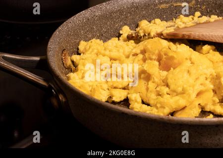 Primo piano di uova strapazzate preparate con una miscela di uova strapazzate a base vegetale alternativa in una padella su una stufa elettrica. Uova di imitazione. Cibo vegano sano. Foto Stock
