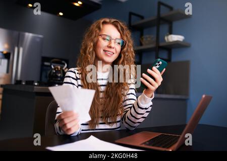 Donna felice che utilizza l'app di online banking per pagare le fatture, tenere assegni. Reddito di contabilità femminile, debiti, prestiti, riceventi per pagare le tasse con fintech Foto Stock