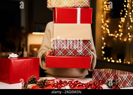 La donna prepara regali per amici e parenti alla vigilia di Natale. La donna tiene il mucchio dei regali nelle scatole del regalo che avvolgono nella carta del mestiere Foto Stock