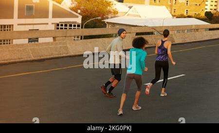 Supportando ogni altra corsa. Ripresa da dietro di un gruppo di joggers che corrono lungo una strada vuota all'alba. Foto Stock