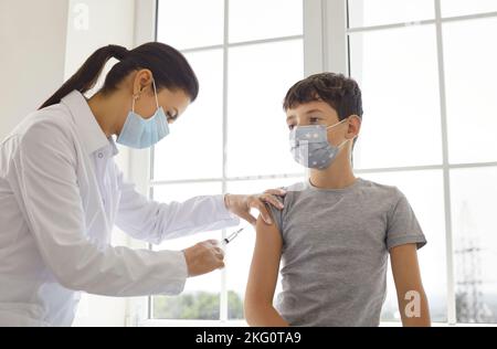 Il medico sta somministrando un'iniezione di vaccino al ragazzo teen in spalla nel concetto di vaccinazione clinica. Foto Stock