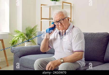 L'anziano non tiene correttamente il telefono fisso e non capisce perché non riesce a sentire nulla. Foto Stock