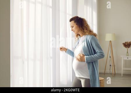 Giovane donna incinta rimanere a casa guardare in finestra Foto Stock