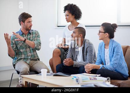 Punti di discussione: Un gruppo di designer diversi che si riunisce intorno a un tavolo da caffè. Foto Stock