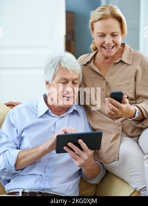 Mobilità moderna. Un uomo anziano felice che utilizza un tablet digitale mentre sua moglie legge un messaggio di testo sul suo cellulare. Foto Stock