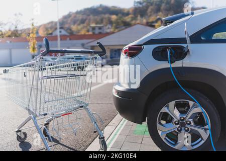 Ricarica di auto elettriche moderne presso il parcheggio del supermercato. Foto Stock