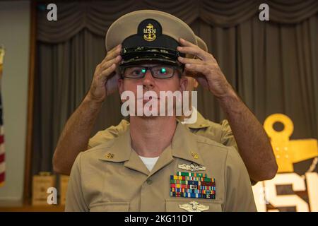 Il Capo Ospedale Corpsman Joshua Wicker, assegnato alla nave di contromisure della miniera USS Warrior (MCM 10), riceve la sua copertura combinata mentre è promosso a capo ufficiale di piccola taglia durante una cerimonia di pinning al Comandante, Fleet Activities Sasebo ottobre 21, 2022. Il rango di Chief Petty Officer è stato creato il 1 aprile 1893, e la cerimonia di pinning del Chief Petty Officer è una tradizione unica per la Marina degli Stati Uniti che significa la promozione a una posizione cruciale di leadership e responsabilità. Foto Stock